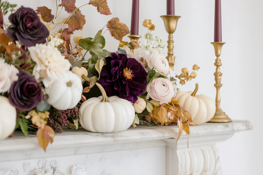Chic autumn mantel decorated with white pumpkins, dark florals, and golden candle holders - Powered by Adobe