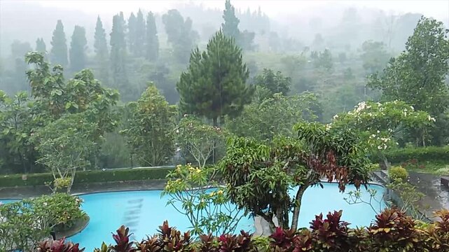 rainfall in the swimming pool with green hills background