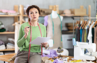 Female tailor businesswoman examines documents, is saddened by results of workshop. Business owner...