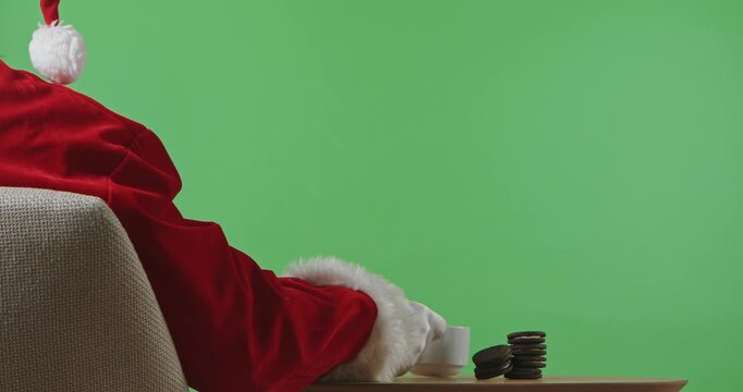 Rear view of Santa Claus is sitting at a table drinking tea with cookies. Isolated on a green background for Christmas and New Year's themes.