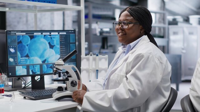 African american chemist analyzing molecular samples in a lab, using professional microscope. Healthcare innovation and biochemistry experiments represent scientific method and discovery.
