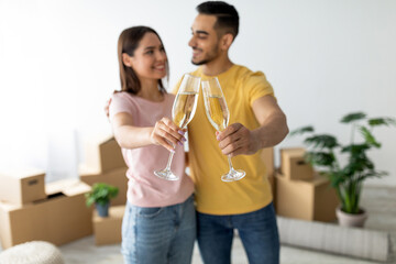A happy couple toasts with champagne glasses in a bright living room surrounded by moving boxes....