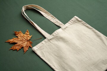 A canvas tote bag with a maple leaf on a dark green background indoors