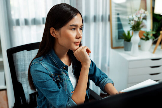 Working young beautiful asian creative manager focusing on pc, creating with new website design on new social media online channel planning with blue jeans shirt at modern home office. Stratagem.