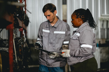 Diverse technician checking used car damaged engine block at scrap yard warehouse recycle area part. Maintenance engineer inspecting rust oily auto motor old spare part in junkyard for reuse service