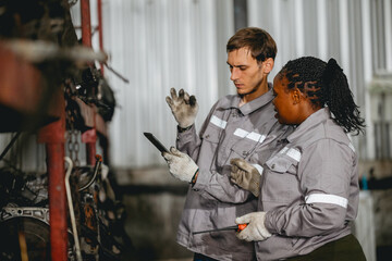 Diverse technician checking used car damaged engine block at scrap yard warehouse recycle area part. Maintenance engineer inspecting rust oily auto motor old spare part in junkyard for reuse service