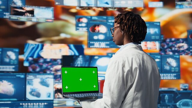 Green screen laptop used by healthcare expert looking at CT scans, MRI data, and lab analytics on videowall. Scientist in medical research lab reading health data with mockup notebook, camera A - Powered by Adobe