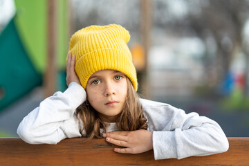 Serious girl in yellow cap with freckles looking at camera, with hand on head in closeup portrait. Intense gaze and neutral expression highlighting features