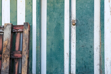 painted with vertical green and white stripes, the texture shows peeling paint and is partially obstructed by a stack of dark wood pallets