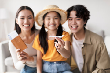 Smiling family poses in a bright living room, excited for their upcoming trip. They hold boarding passes and a toy airplane, showcasing their travel plans and family bond.