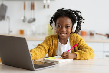 A young girl enjoys her online learning experience, wearing headphones and taking notes with a...