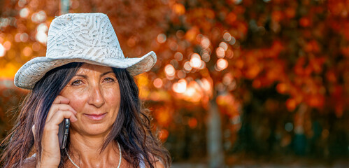 Happy woman with cowboy hat surrounded by colorful fall leaves in the backyard