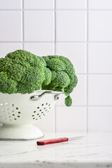 Raw broccoli in a white enamel colander