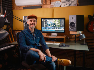 Male video editor smiling at camera while seated at editing workstation with professional audio equipment