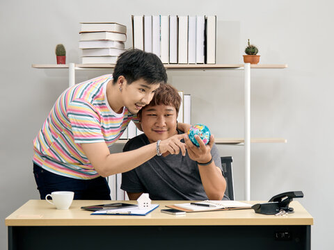 Asian gay couple looking at globe together at desk in home office. Concept of LGBTQ+ relationship, global vision, travel planning, world awareness, diversity, and working towards shared dreams