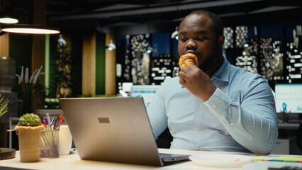African american professional overeating and working late at night, serving unhealthy food and dealing with a compulsive eating disorder due to overtime and constant tension. Mental health.