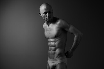 Fototapeta premium A toned man poses confidently in black and white, showcasing a strong physique with emphasis on muscles, creating a dramatic and artistic presence.
