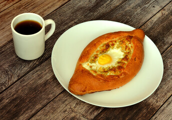 Adjarian khachapuri with egg and cheese and a cup of hot tea on a wooden table.
