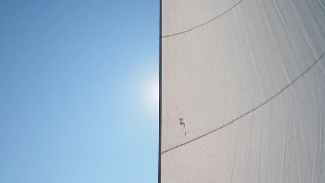 Panning down the mast of a sailboat showing a full jib  on port tack seen from the stern