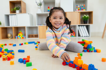 toddler girl playing building blocks or plastic bricks toy at home