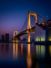 Obraz premium Stunning View of the Legendary Rainbow Bridge in Tokyo, Japan Glowing at Dusk Over the Water