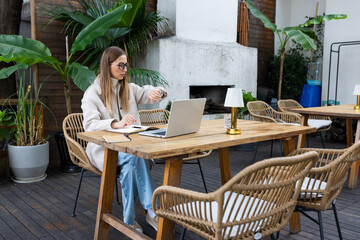 Young woman working on laptop and checking time at outdoor cafe