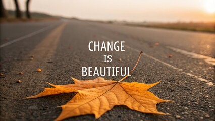 A vibrant golden autumn leaf lies on a dark asphalt road with the motivational text Change is Beautiful