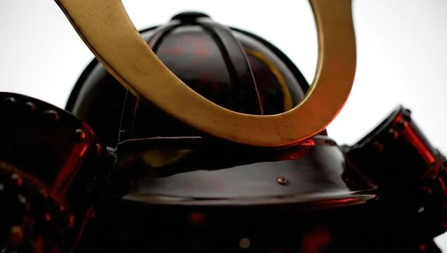 Detailed macro photo of a Japanese samurai kabuto helmet, highlighting its reflective dark lacquer and ornate golden maedate crest against a white background
