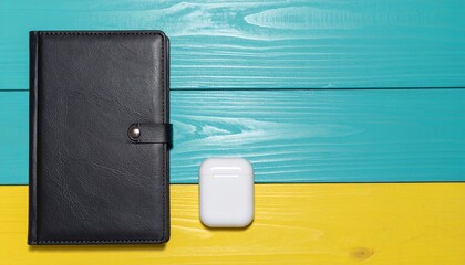 Modern Essentials Black Planner and White Earbuds on Contrasting Teal and Yellow