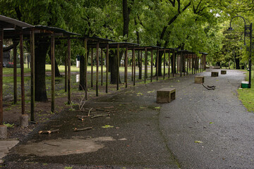A covered wooden pergola structure with vertical beams runs alongside a paved pathway through a...