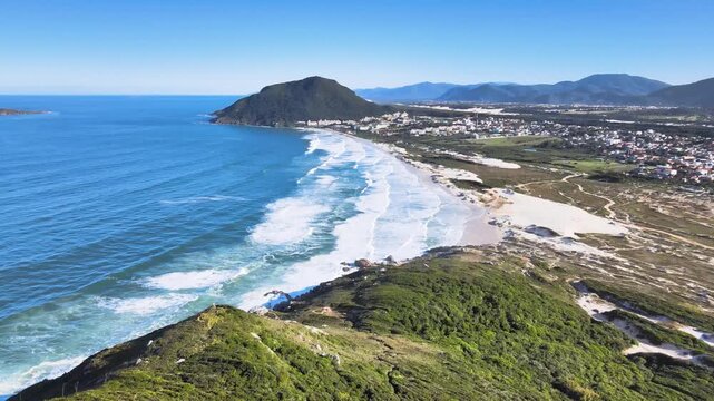 Panoramic aerial view of Santinho beach and Aranhas Island, restinga area and dunes seen from the top of Ingleses hill on a beautiful sunny summer day.