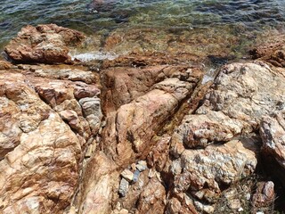 Beautiful rocky seashore with golden-brown stones and clear blue sea. Perfect for nature, geology, and coastal travel photography. Peaceful and scenic seaside landscape background.