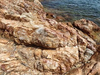 Beautiful rocky seashore with golden-brown stones and clear blue sea. Perfect for nature, geology, and coastal travel photography. Peaceful and scenic seaside landscape background.
