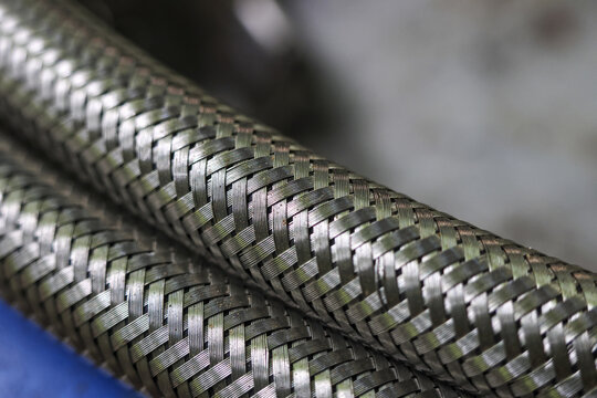 Close up of braided metal hose with silver steel texture. This industrial pipe or tube shows strength and durability in detail, perfect for engineering or plumbing concepts