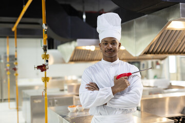 Confident male chef in white uniform standing with arms crossed in modern kitchen. Concept of...