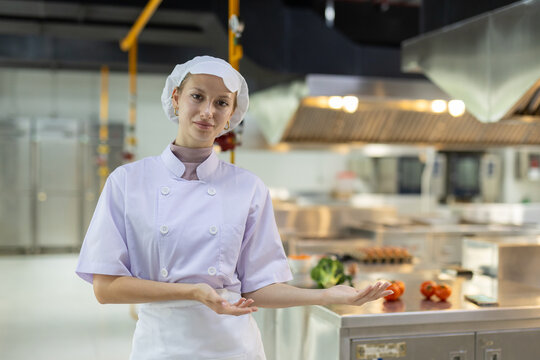 Female chef in professional uniform presenting kitchen counter with fresh vegetables. Concept of food preparation, healthy cooking, culinary arts and commercial kitchen environment. - Powered by Adobe