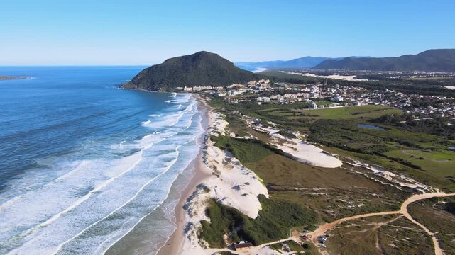 Panoramic aerial view of Santinho beach and Aranhas Island, restinga area and dunes seen from the top of Ingleses hill on a beautiful sunny summer day.