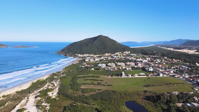 Panoramic aerial view of Santinho beach and Aranhas Island, restinga area and dunes seen from the top of Ingleses hill on a beautiful sunny summer day.