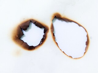 Close up of a fire burned hole on white paper background. Paper burn mark stain and damaged texture. A piece of scorched and torn paper with a fire burned hole and black scorch marks with stain.