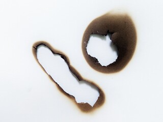 Close up of fire damaged hole on white paper background. Paper burn mark with black stain texture. White paper with fire burned hole.