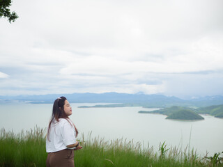 Confident curvy Asian woman smiling in nature with lake and mountain background.
