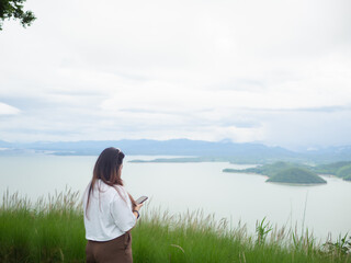 Confident curvy Asian woman smiling in nature with lake and mountain background.