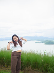 Confident curvy Asian woman smiling in nature with lake and mountain background.