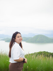 Confident curvy Asian woman smiling in nature with lake and mountain background.