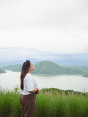 Confident curvy Asian woman smiling in nature with lake and mountain background.