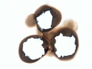 Fire burned hole on white paper background close up. Burn mark stain and rough paper texture detail. Burnt paper.