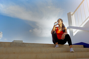 Tired runner woman with a bottle of electrolyte drink freshness after training outdoor workout at the stadium stairway.