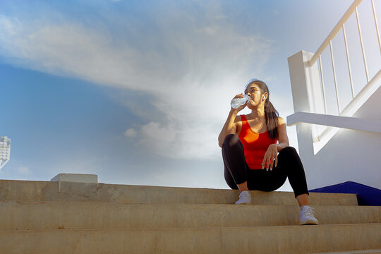Tired runner woman with a bottle of electrolyte drink freshness after training outdoor workout at the stadium stairway.