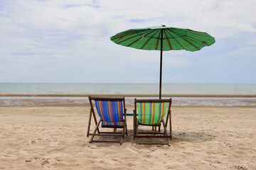 Two chairs are placed on the sandy beach with a parasol, overlooking the clear sky and sea.