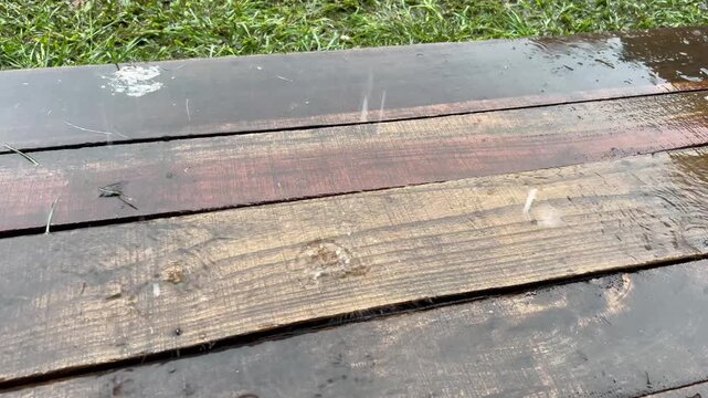 Heavy rain falling on wet wooden deck boards beside green grass.